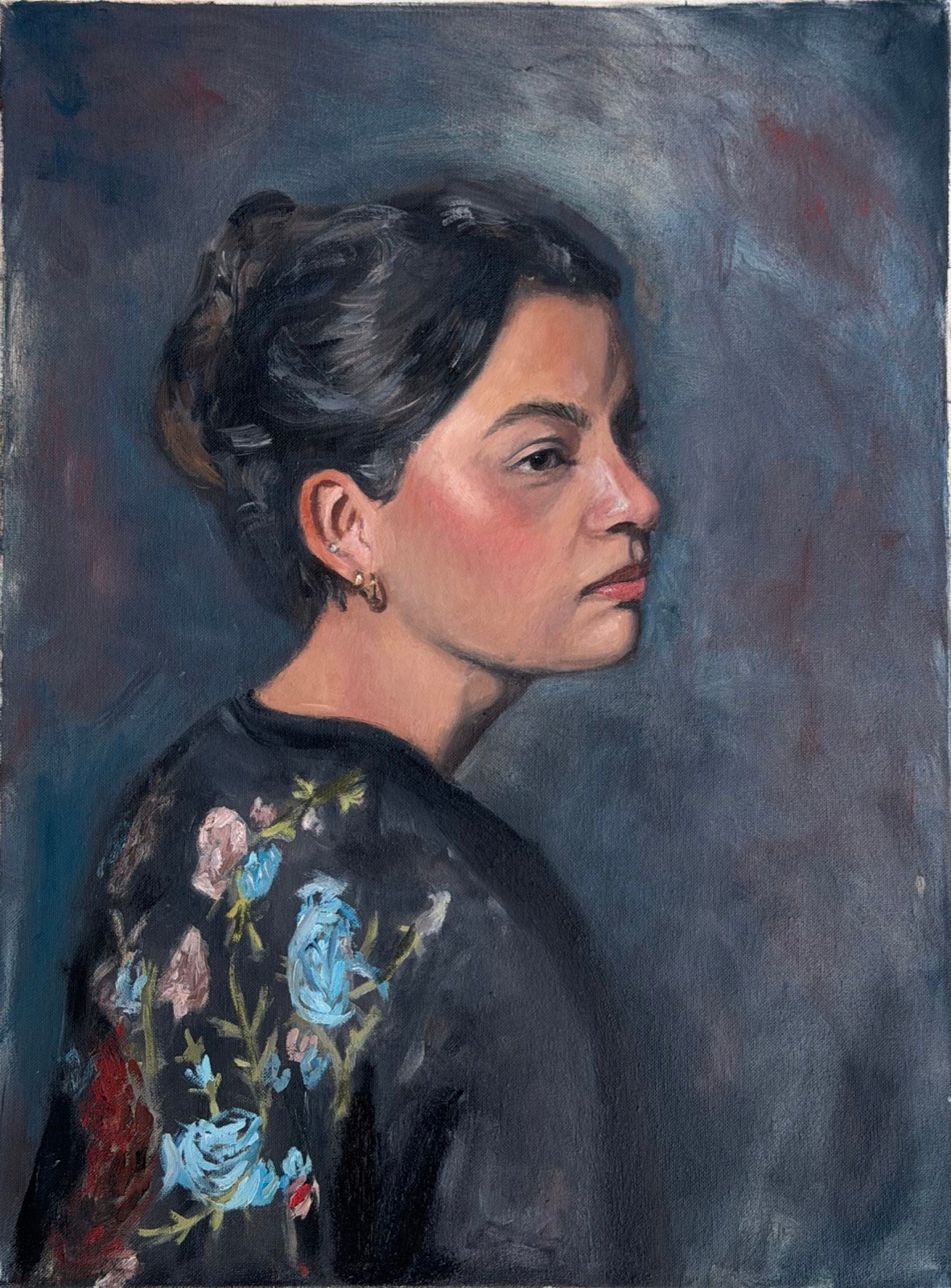 Portrait of a woman seen in profile, dark hair pinned up, wearing a dark top embroidered with pink and blue flowers, against a grey-blue ground