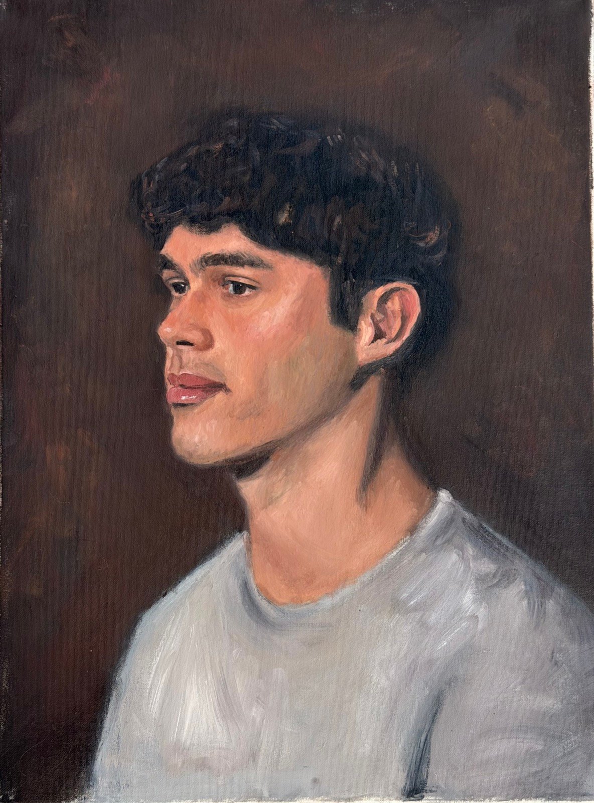 Profile portrait of a young man with dark curly hair in a white t-shirt, against a warm brown ground