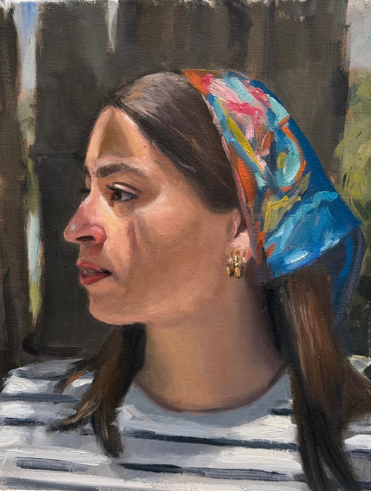 Profile portrait of a woman wearing a brightly patterned headscarf in pink, blue and orange over a black-and-white striped shirt, against an olive ground