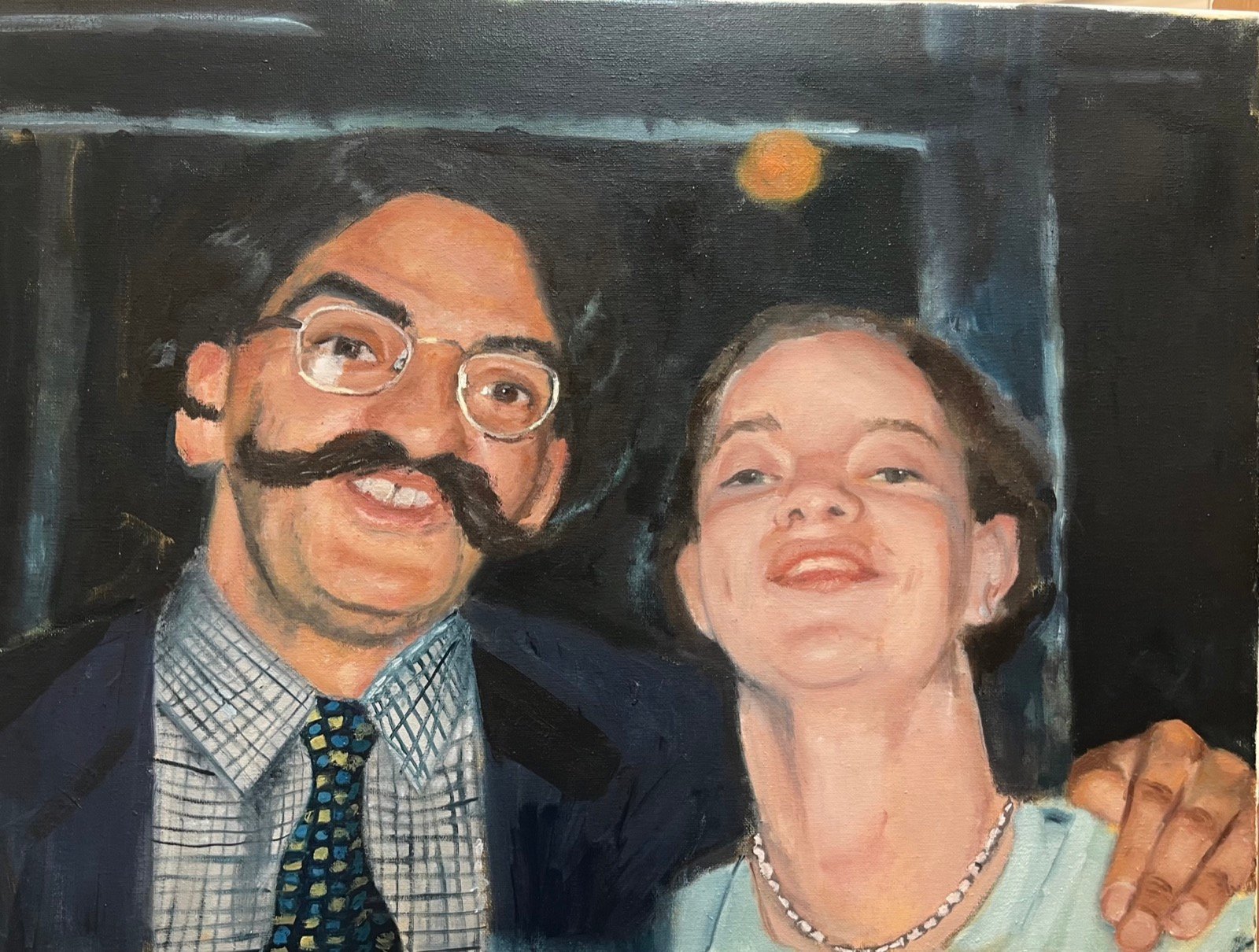 Double portrait of a smiling man in wire glasses with a large dark moustache, his arm around a woman in a pale blue top, against a dark interior